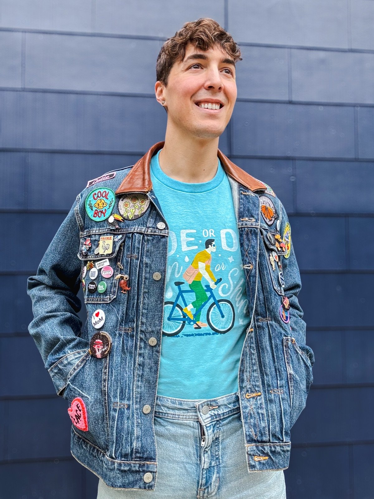 Joshua Goupil, founder of Wug Prints, smiling outdoors in a denim jacket covered in pins